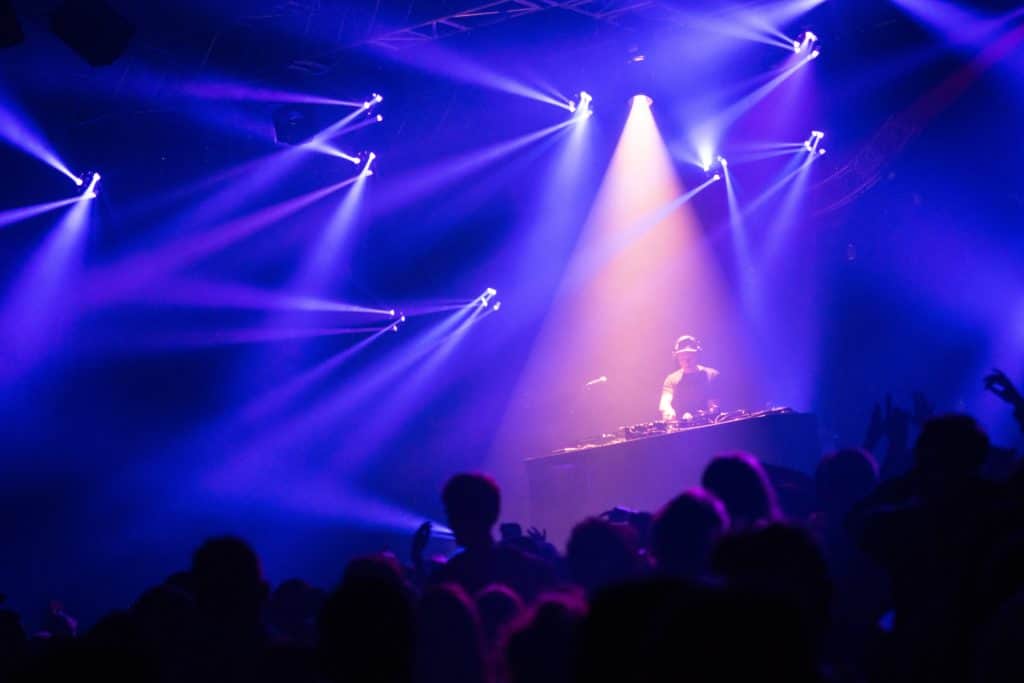 A DJ performing on stage in front of a big party crown of party goers