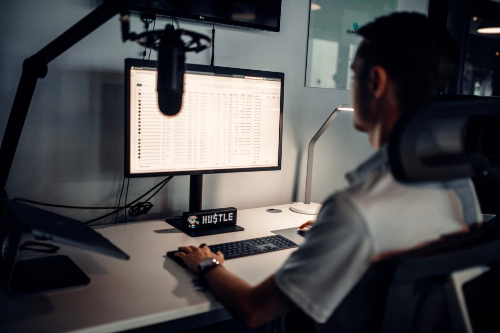 A man uses a blue yeti microphone to record in front of a computer.