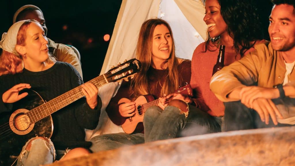 Friends on a camping trip singing songs and playing guitar and ukulele